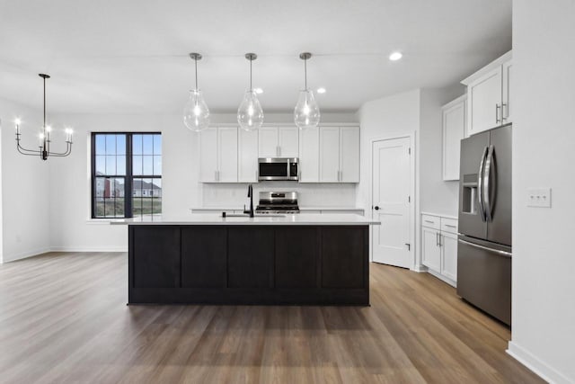 kitchen with pendant lighting, a kitchen island with sink, stainless steel appliances, and white cabinets