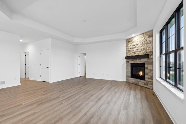 unfurnished living room with a stone fireplace, light hardwood / wood-style floors, and a tray ceiling