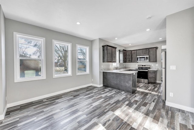 kitchen with sink, appliances with stainless steel finishes, hardwood / wood-style floors, dark brown cabinets, and kitchen peninsula