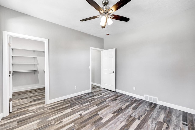 unfurnished bedroom featuring ceiling fan, dark hardwood / wood-style flooring, a closet, and a walk in closet