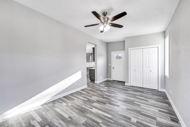 unfurnished bedroom featuring connected bathroom, a closet, hardwood / wood-style flooring, ceiling fan, and multiple windows