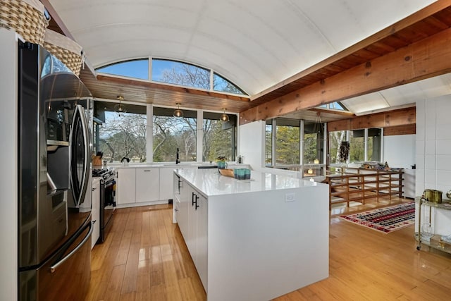 kitchen with lofted ceiling with skylight, a kitchen island, white cabinetry, stainless steel fridge, and gas stove