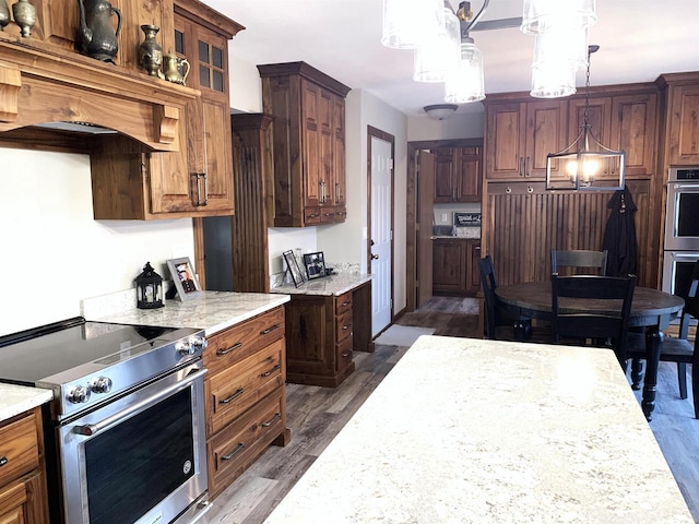 kitchen with dark wood-type flooring, premium range hood, appliances with stainless steel finishes, light stone counters, and decorative light fixtures