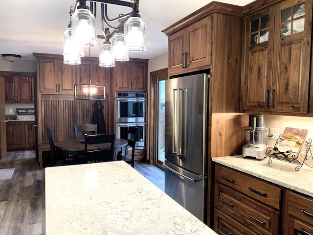 kitchen featuring appliances with stainless steel finishes, dark wood-type flooring, pendant lighting, and light stone counters