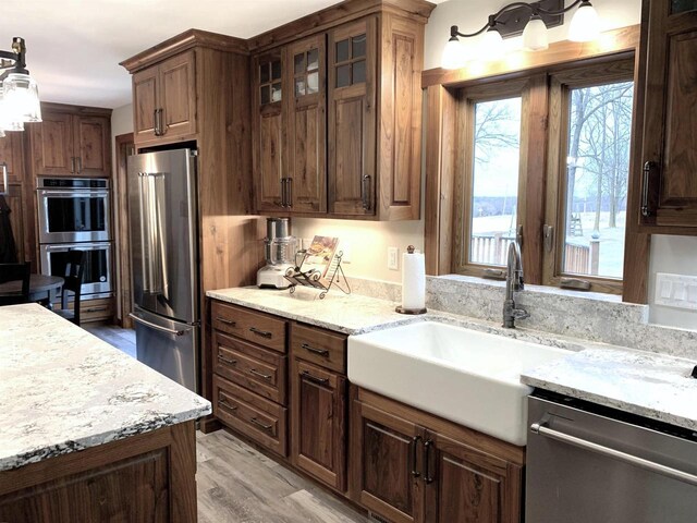 kitchen featuring sink, decorative light fixtures, stainless steel appliances, light stone countertops, and light hardwood / wood-style floors
