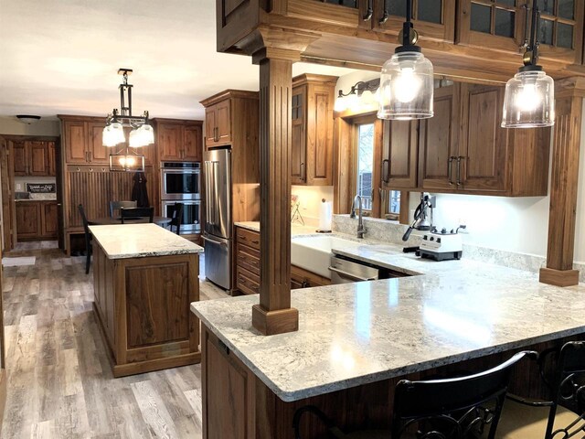 kitchen featuring a kitchen bar, light stone counters, hanging light fixtures, stainless steel appliances, and light hardwood / wood-style floors