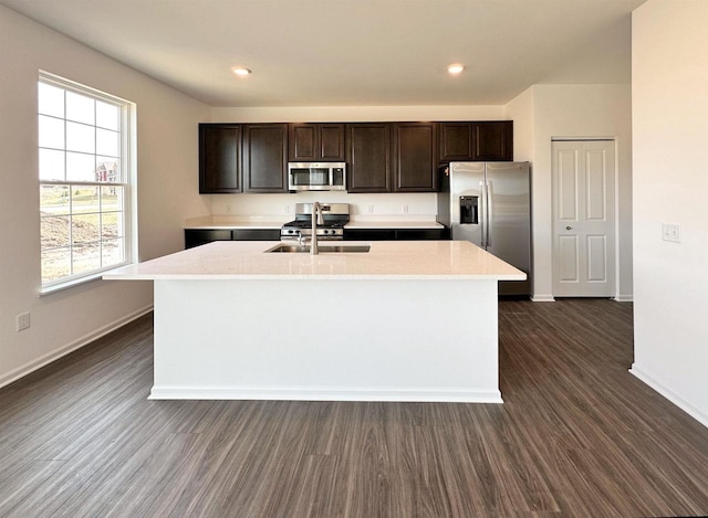 kitchen with dark wood finished floors, an island with sink, stainless steel appliances, dark brown cabinets, and light countertops