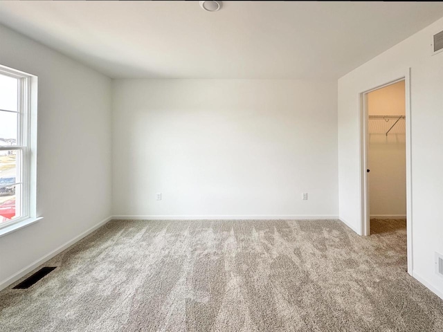 carpeted empty room featuring a wealth of natural light, visible vents, and baseboards