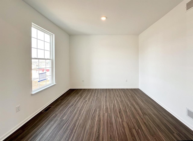 spare room with dark wood-style floors, visible vents, and baseboards