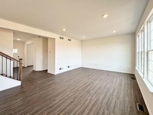 empty room with visible vents, dark wood finished floors, and stairway