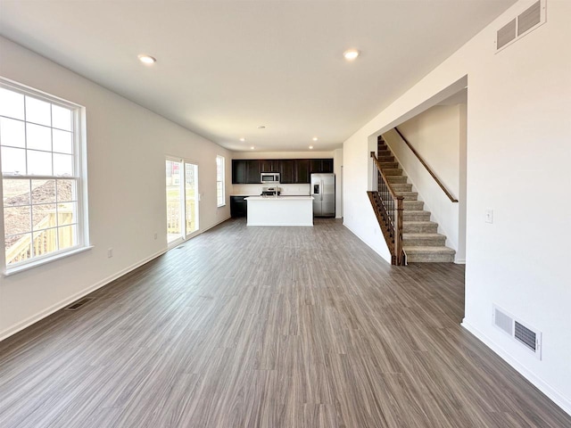 unfurnished living room with wood finished floors, visible vents, and stairs