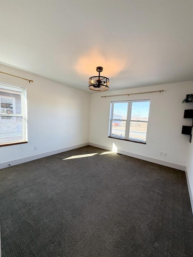 unfurnished room with dark colored carpet and a notable chandelier