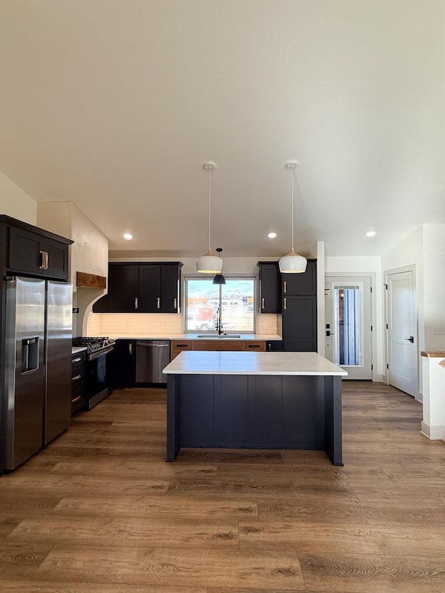 kitchen with appliances with stainless steel finishes, decorative light fixtures, sink, a center island, and light wood-type flooring