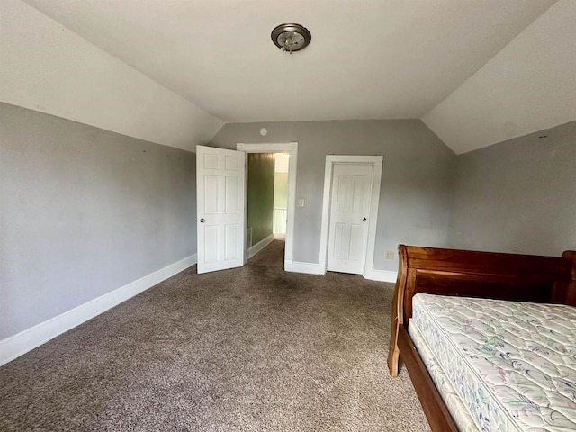 unfurnished bedroom with vaulted ceiling and dark colored carpet