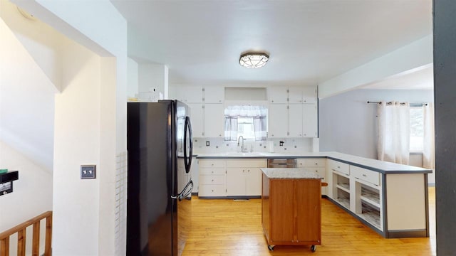 kitchen featuring sink, black refrigerator, plenty of natural light, a kitchen island, and white cabinets