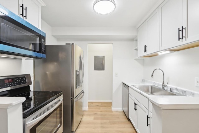 kitchen with appliances with stainless steel finishes, sink, white cabinets, and light hardwood / wood-style floors