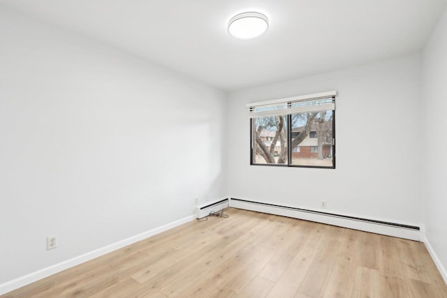 spare room featuring a baseboard heating unit and light hardwood / wood-style floors