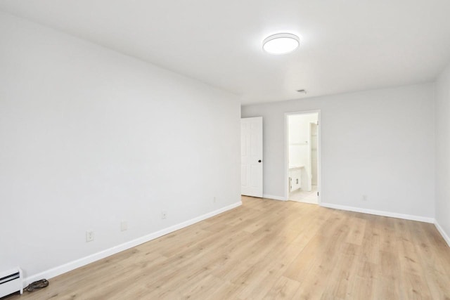 empty room featuring light wood-type flooring and a baseboard heating unit