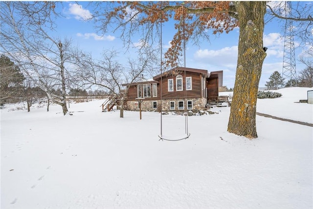 snow covered back of property featuring stone siding