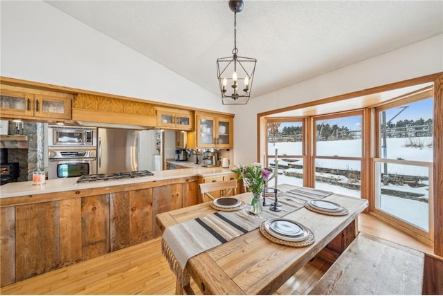 dining room with light hardwood / wood-style flooring, a notable chandelier, a textured ceiling, vaulted ceiling, and a wood stove