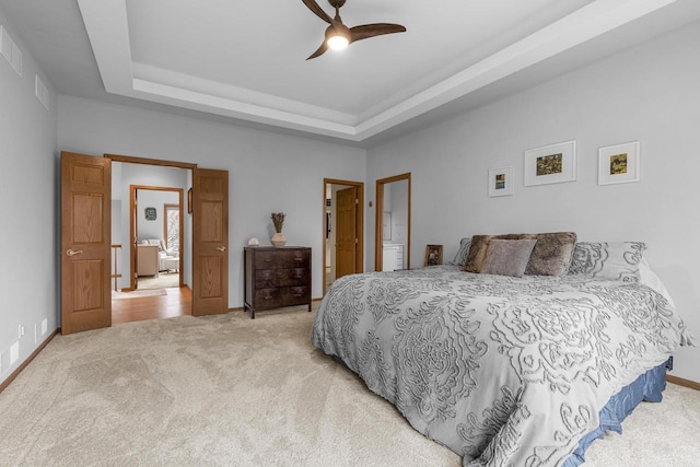 bedroom with a tray ceiling, light colored carpet, and ceiling fan