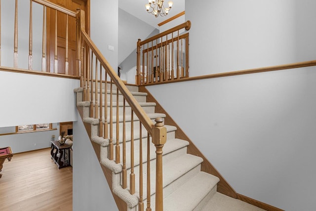 stairway featuring an inviting chandelier, a towering ceiling, and hardwood / wood-style flooring