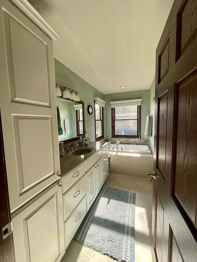 bathroom with tiled tub, vanity, and tile patterned flooring