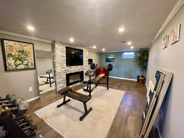 exercise area with ornamental molding, a stone fireplace, a textured ceiling, and dark hardwood / wood-style flooring