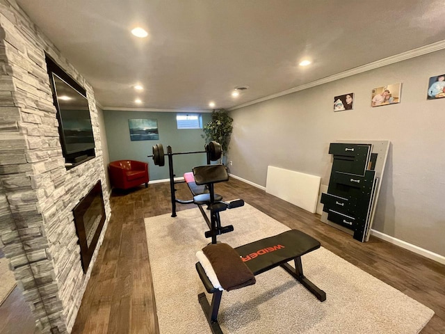 exercise room featuring ornamental molding, a stone fireplace, and dark hardwood / wood-style flooring