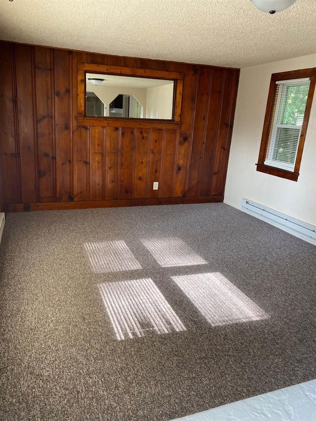 empty room featuring baseboard heating, carpet flooring, a textured ceiling, and wood walls