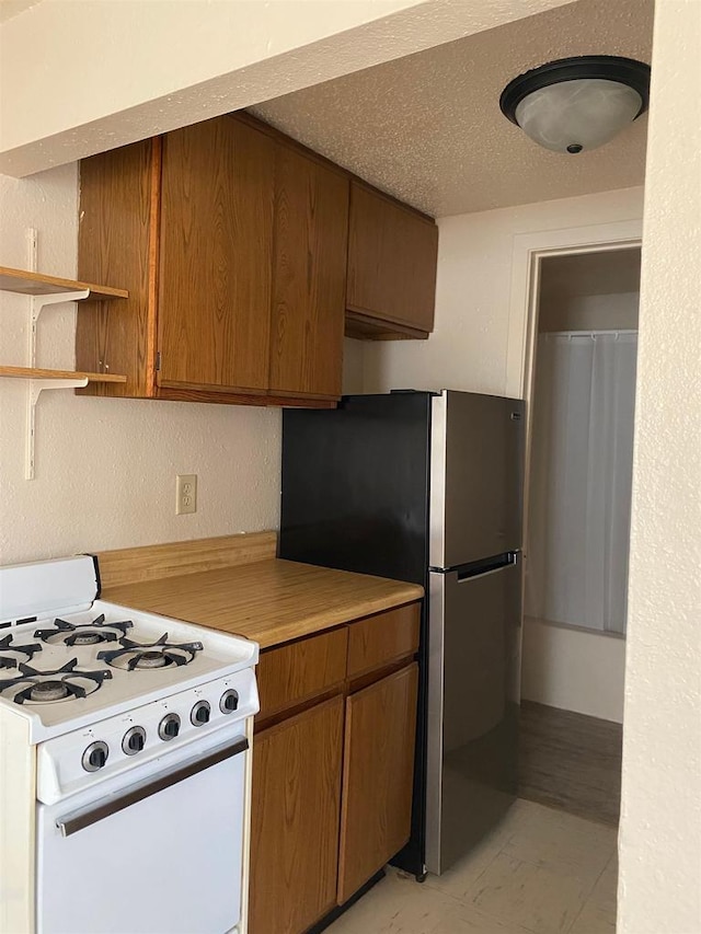 kitchen with white range with gas cooktop, stainless steel fridge, and a textured ceiling