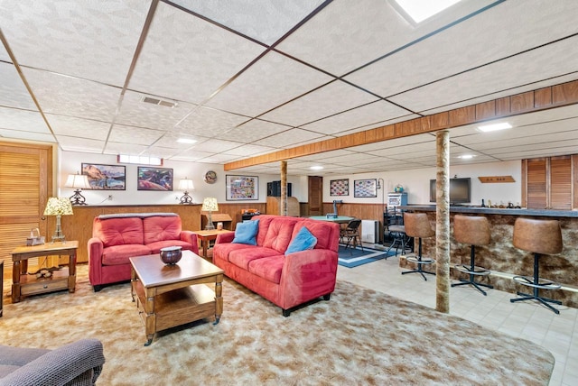 living room with a paneled ceiling, bar area, and wooden walls