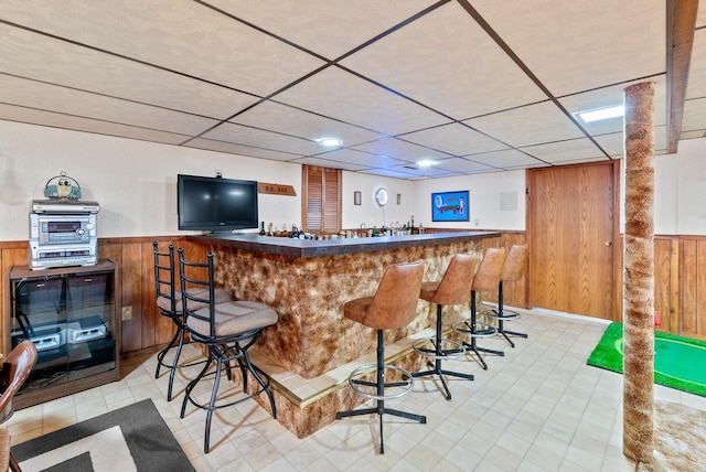 bar featuring a drop ceiling and wood walls