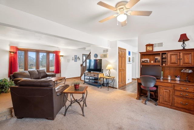 carpeted living room featuring built in desk and ceiling fan