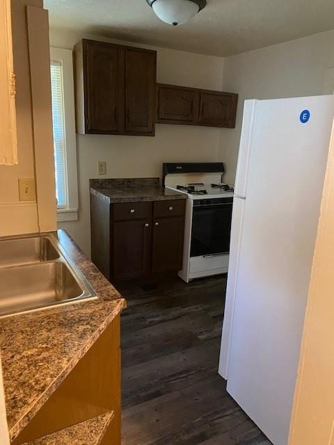 kitchen with dark brown cabinetry, sink, white appliances, and dark hardwood / wood-style flooring