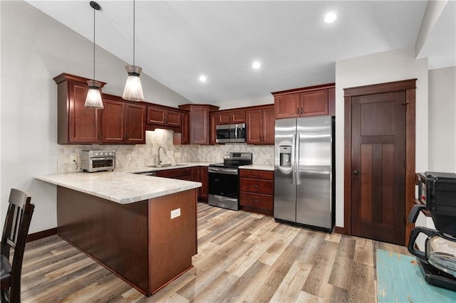 kitchen featuring appliances with stainless steel finishes, pendant lighting, sink, light hardwood / wood-style floors, and kitchen peninsula