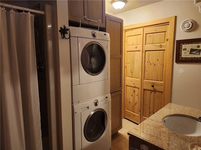 laundry area with stacked washer / drying machine, sink, and light tile patterned floors