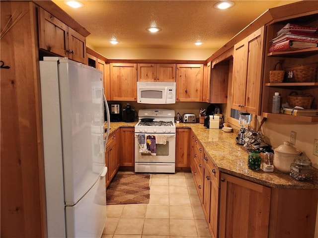 kitchen featuring light stone counters, white appliances, a textured ceiling, and light tile patterned floors