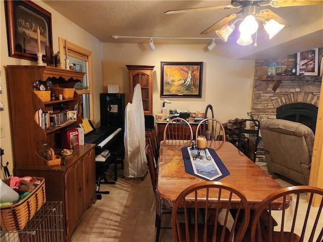 tiled dining space with ceiling fan, a fireplace, rail lighting, and a textured ceiling