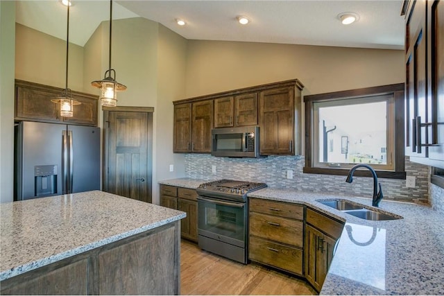 kitchen with appliances with stainless steel finishes, decorative light fixtures, lofted ceiling, sink, and light stone countertops