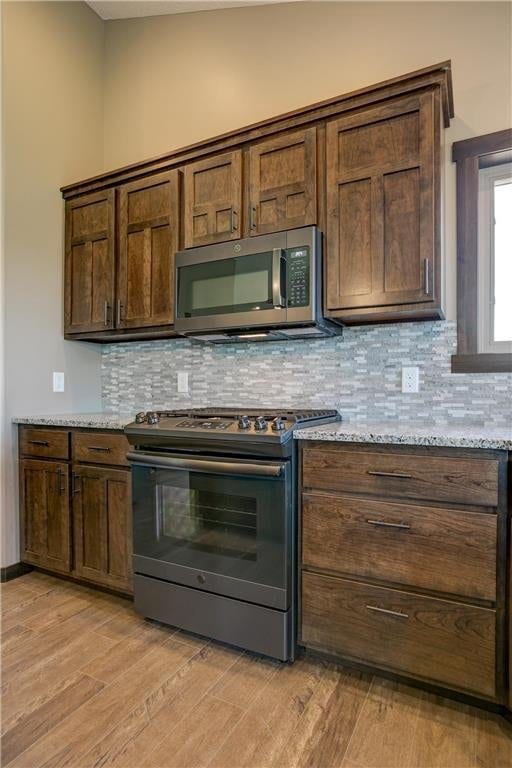 kitchen with appliances with stainless steel finishes, dark brown cabinets, light stone counters, light hardwood / wood-style floors, and decorative backsplash