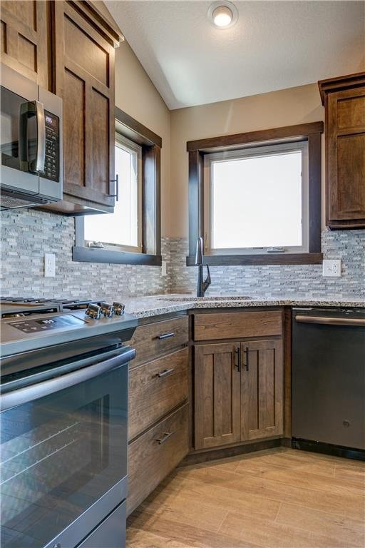 kitchen with appliances with stainless steel finishes, light stone countertops, sink, and light wood-type flooring