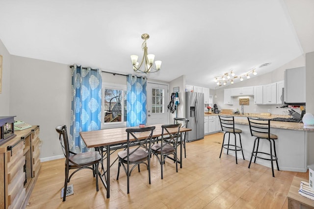 dining room with a notable chandelier, vaulted ceiling, and light wood-type flooring