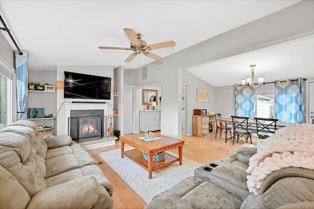 living room with vaulted ceiling, ceiling fan with notable chandelier, and light wood-type flooring