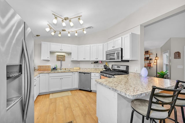 kitchen with appliances with stainless steel finishes, sink, a breakfast bar area, white cabinets, and kitchen peninsula