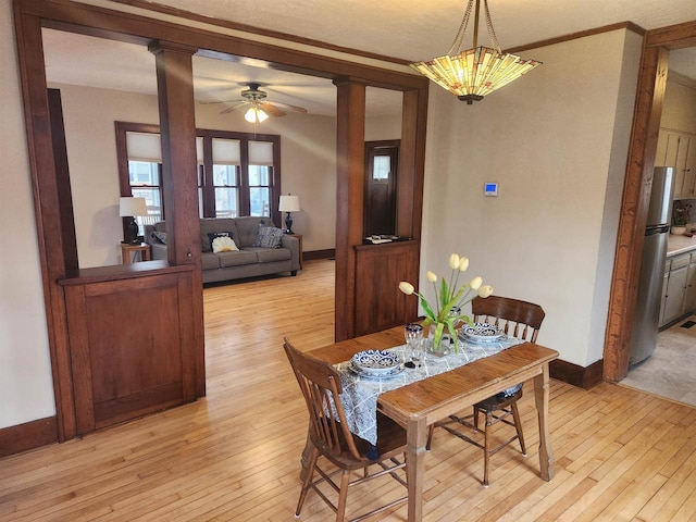 dining space with decorative columns, ornamental molding, ceiling fan, and light hardwood / wood-style flooring