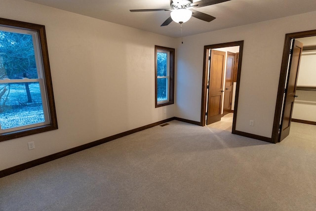 unfurnished bedroom featuring ceiling fan, light colored carpet, a spacious closet, and ensuite bath