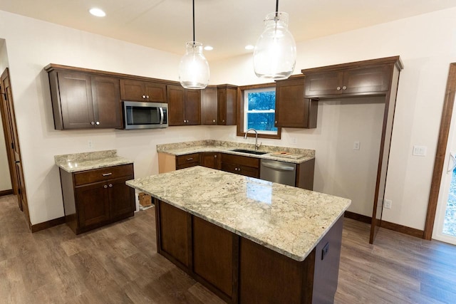 kitchen featuring a kitchen island, pendant lighting, sink, light stone counters, and stainless steel appliances