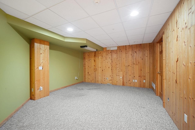 basement featuring carpet, a drop ceiling, and wood walls