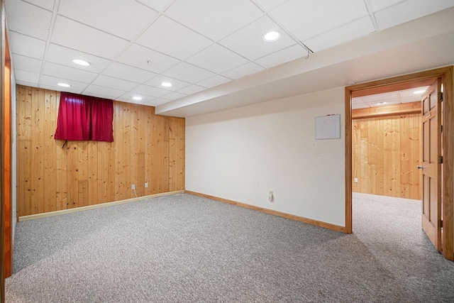 basement featuring carpet, a paneled ceiling, and wooden walls